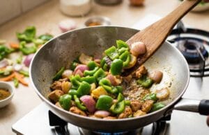 Sautéing vibrant green bell peppers and chopped onions in a wok for a quick Chicken Manchurian stir-fry, keeping the vegetables crunchy on high heat.