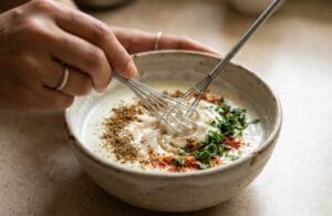 Mixing spices and herbs into yogurt to prepare Zeera Raita."