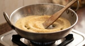 Ghee mein bhoonti hui daane-dar Suji,Homemade Halwa Puri Recipe banane ke liye, upar Elaichi aur chamach.