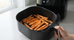 A close-up of raw potato sticks arranged in a single, even layer inside an air fryer basket, ready to cook into delicious Crispy Air Fryer Sweet Potato Fries.