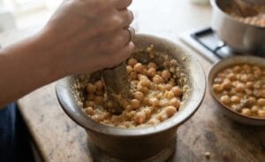 Crushing a portion of boiled chickpeas in a traditional mortar and pestle to create a thick and creamy texture for the Authentic Lahori Chana Recipe.
