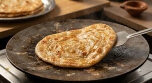 A golden-brown, crispy paratha being toasted on a tawa for a delicious Shami Kabab Paratha Roll