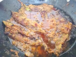 Frying karela peels with tomatoes and green chilies, then combining with stuffed karele and reserved masala for Masala Bharre Karele recipe.